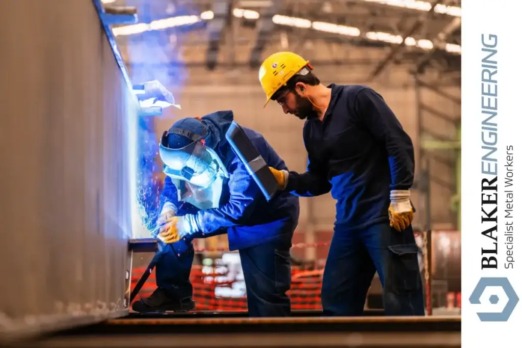 Welder working on metal with supervisor overseeing, supporting the next generation through apprenticeships.