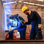 Welder working on metal with supervisor overseeing, supporting the next generation through apprenticeships.
